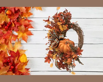 A grapevine wreath filled with lush autumn greenery and focal pumpkin. The wreath hangs on a white panel wall.