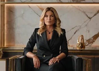 Confident businesswoman with blonde hair wearing a black suit, seated in a luxurious office with marble and gold accents