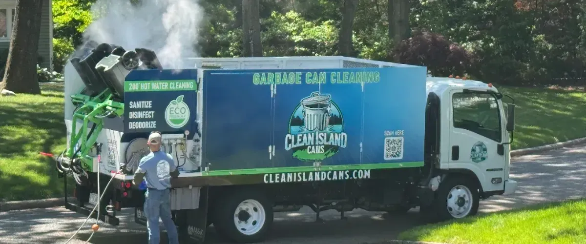 Clean Island Cans truck cleaning garbage bins with hot water and steam, operated by a uniformed technician in a residential neighborhood.
