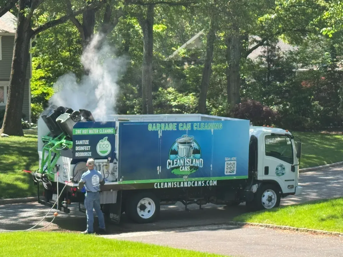 Clean Island Cans truck releasing steam while cleaning residential trash bins on a driveway in a suburban neighborhood.