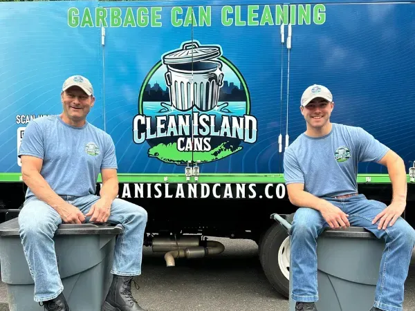 Clean Island Cans crew sitting on trash bins in front of their garbage can cleaning truck, smiling at the camera. 