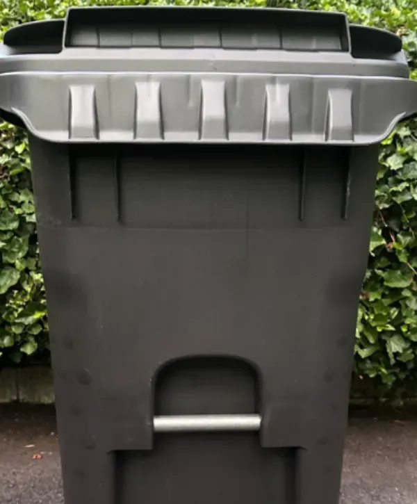 Large black durable trash can with reinforced design placed outdoors