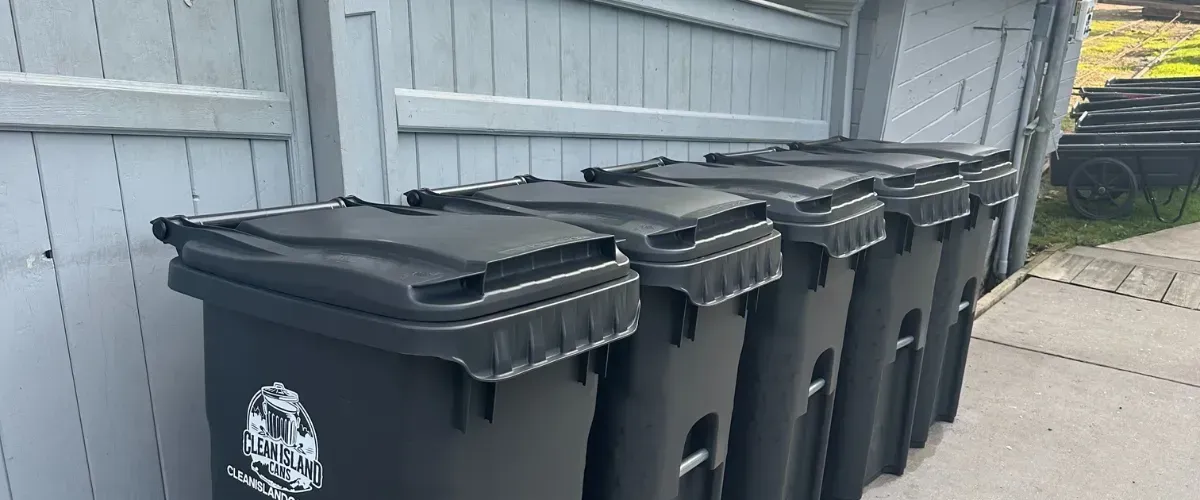 Row of Clean Island branded trash bins neatly lined up along a wooden fence