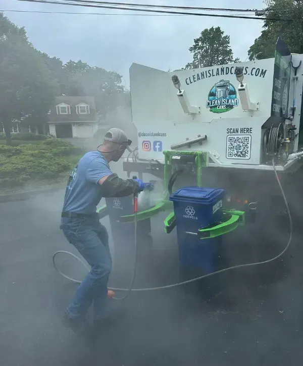 Technician using cleaning truck system to sanitize blue recycling bins with steam and water spray