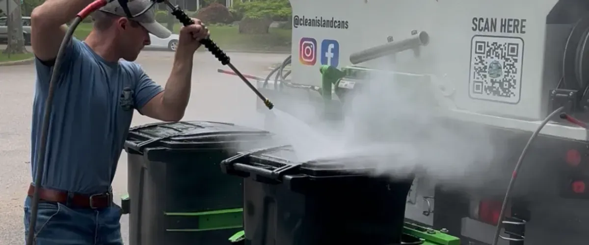 Technician power washing trash bins with high-pressure water system for sanitation