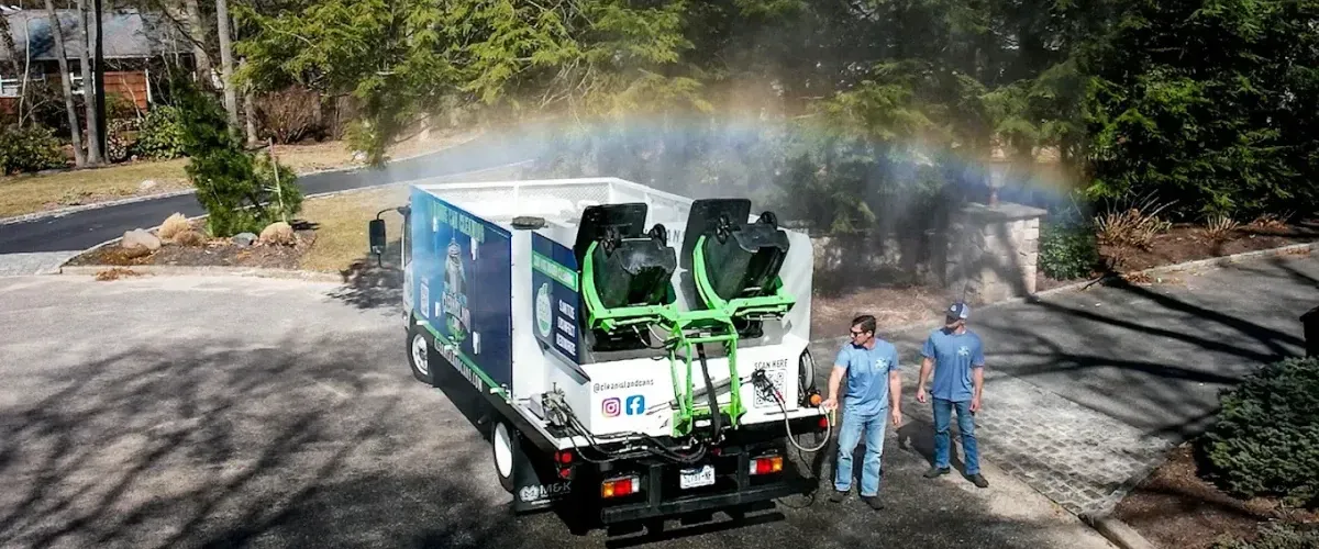 Professional trash bin cleaning service with truck spraying water under a rainbow mist.