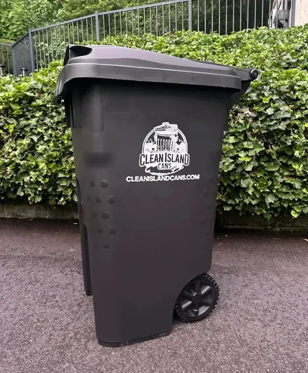 Clean black trash bin with company logo placed outdoors near a hedge.