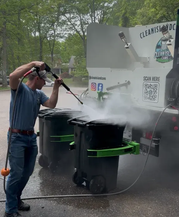 Technician pressure washing garbage bins during curbside cleaning service.