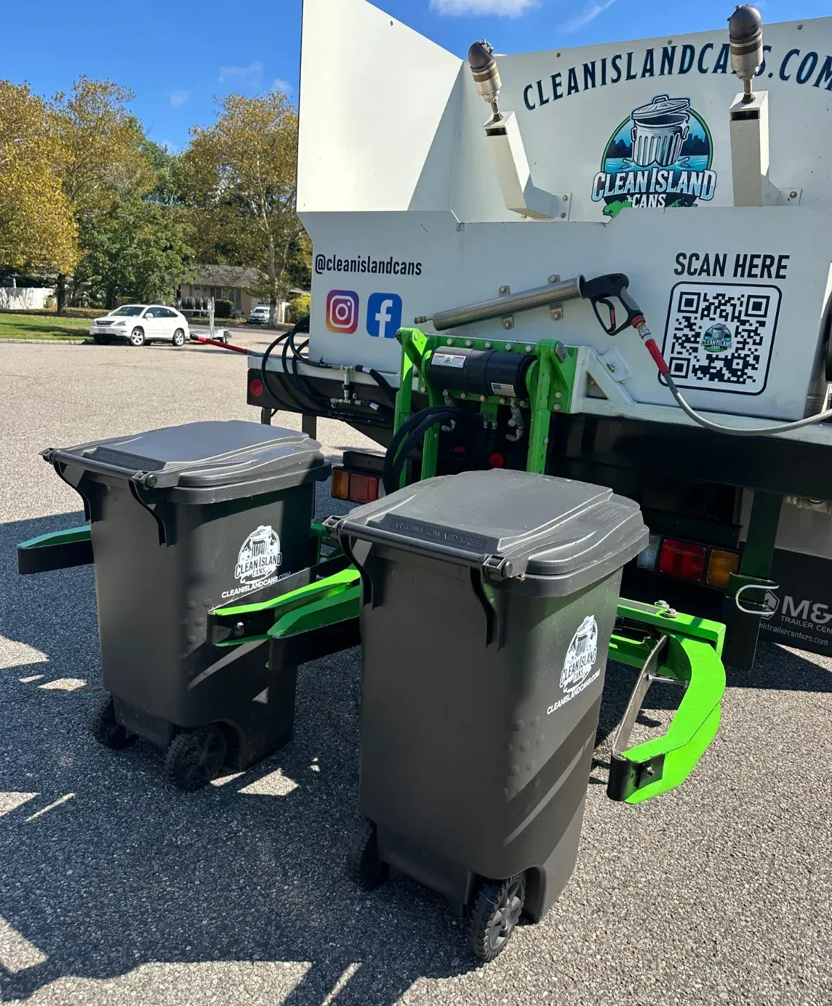 A Clean Island Cans garbage can cleaning truck parked on a paved driveway with blue and gray bins nearby.