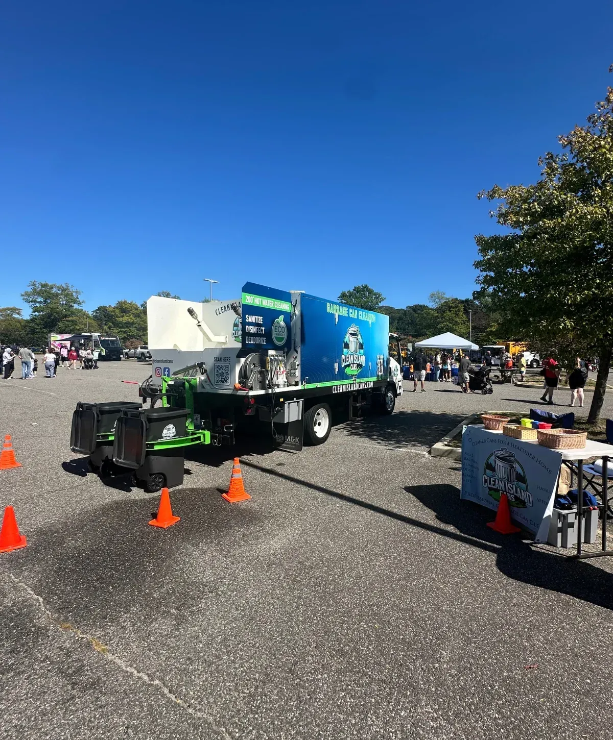 A blue and white Clean Island Cans truck with sanitation equipment parked at an outdoor event on a sunny day.