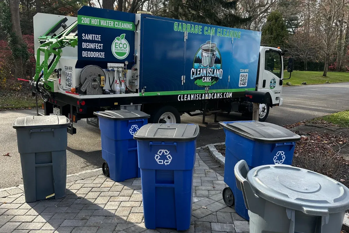 A Clean Island Cans garbage can cleaning truck parked on a paved driveway with blue and gray bins nearby.