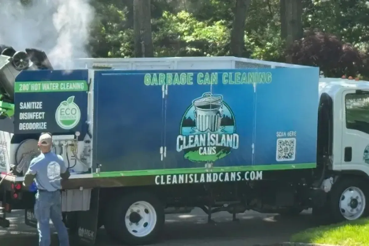 A 'Clean Island Cans' truck with a worker cleaning a garbage can with hot water, producing steam from the cleaning process.