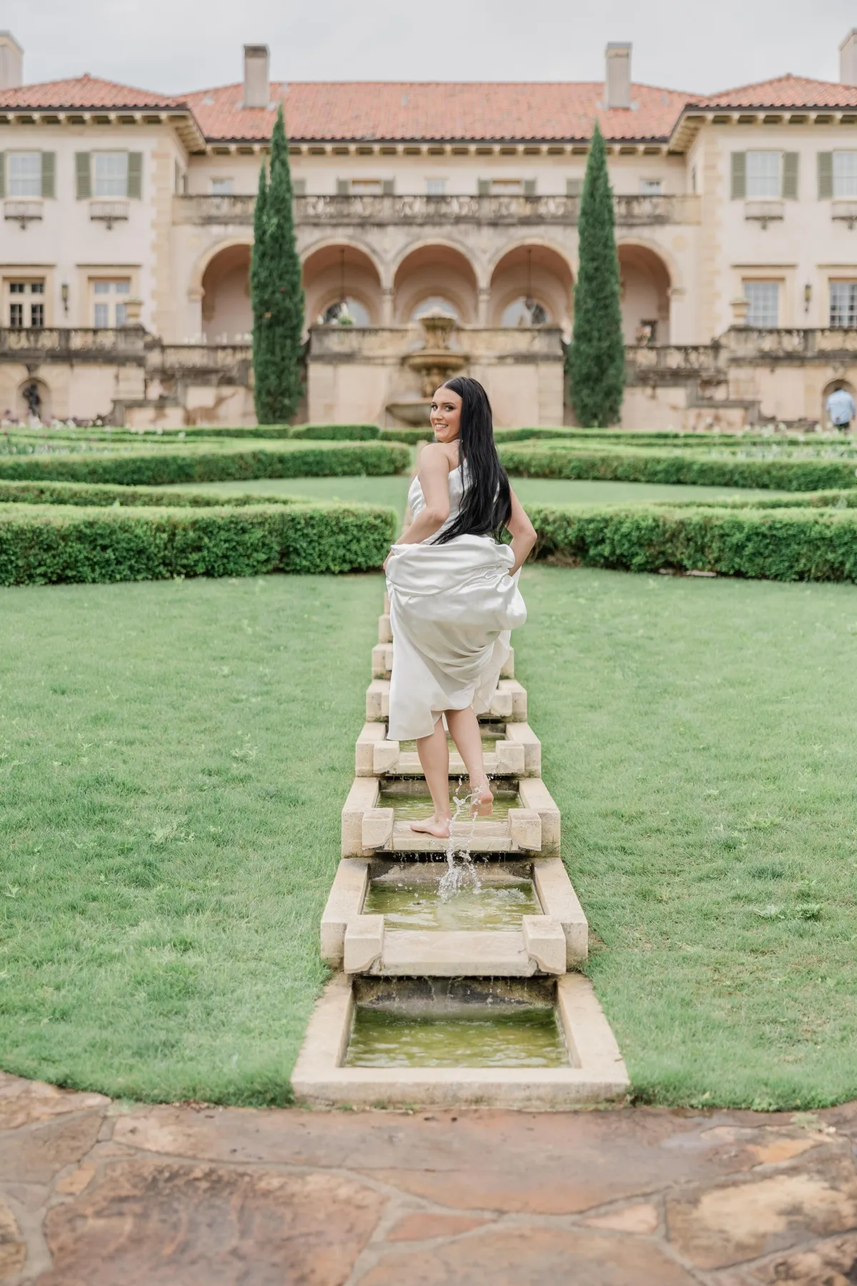 Image of a bride playing in the step waterfall located in the gardens of The Philbrook Museum of Art, Tulsa, Ok. Captured by wedding photographer in Dallas, Arlene Stepanian.