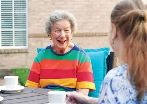 A caregiver and an older female resident smiling and playing a board game together at a table in a cozy room.