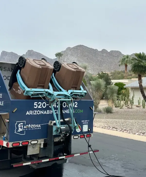  Rear view of Arizona Bin Cleaners truck lifting two brown garbage bins for eco-friendly sanitation near desert-style homes.