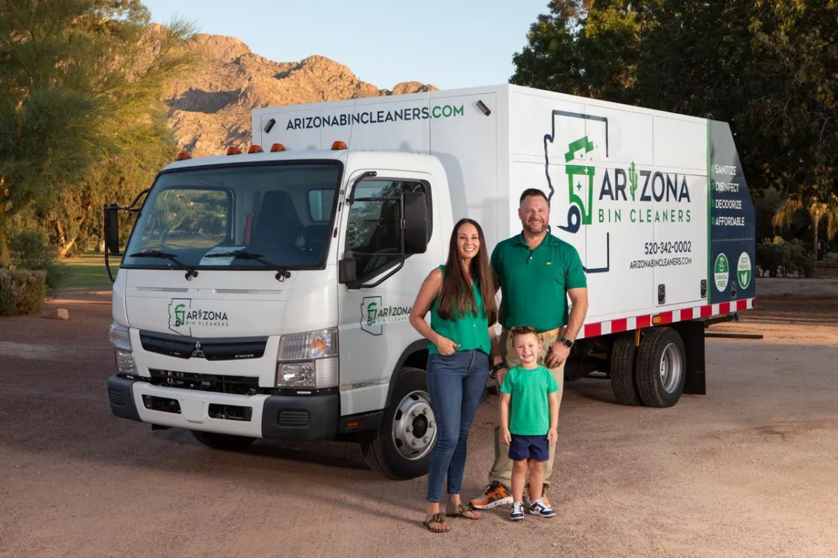 The Fair family standing in front of their Arizona Bin Cleaners truck with two bins lifted for cleaning in a scenic Tucson setting.