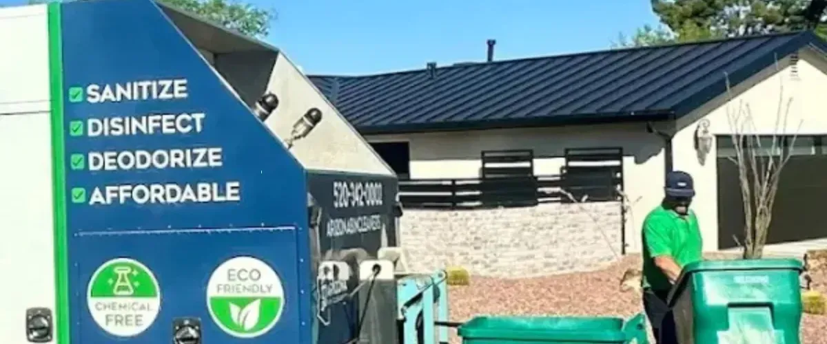 Worker using an eco-friendly bin cleaning truck to sanitize trash bins outside a residential home.