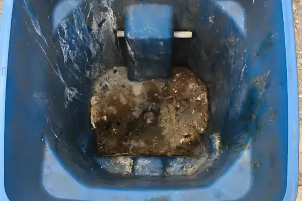 A top-down view inside a dirty, scraped blue plastic trash can with a dried, muddy substance at the bottom.