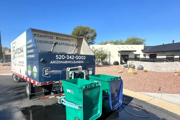 A man in a green shirt places a green trash bin into an Arizona Bin Cleaners truck outside a modern home.