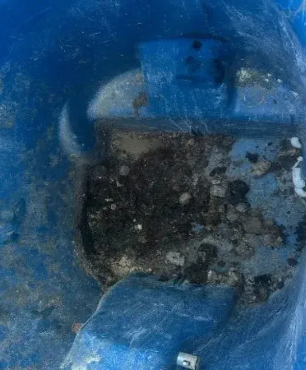 A top-down view of a dirty blue plastic basin, filled with dark grime, debris, and some water.