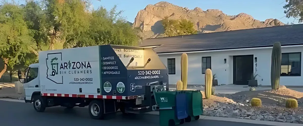 Rear view of a white Arizona Bin Cleaners truck with sanitation equipment and green trash bins in a desert landscape.