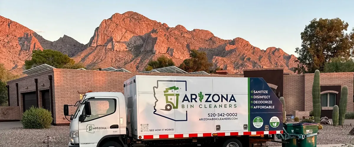 An Arizona Bin Cleaners truck parked in front of brick houses, saguaro cacti, and mountains lit by a sunset.