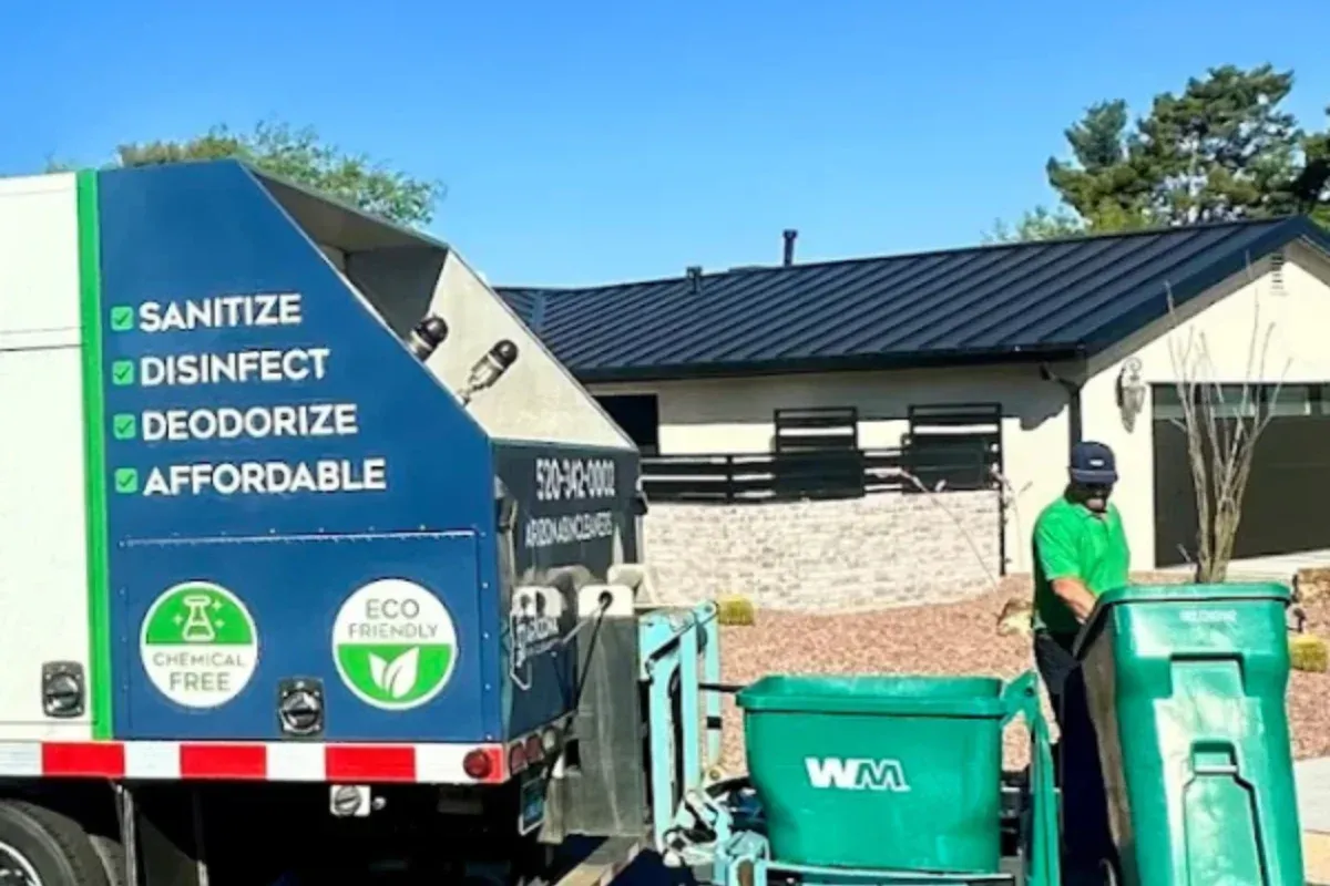 A sanitation truck with cleaning services advertised on its side, next to a worker operating green bins on a sunny day.