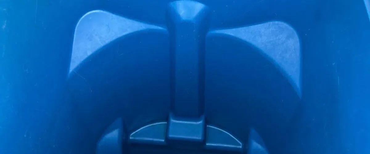 A top-down view inside a clean, empty blue plastic bin or wheeled trash can with a small puddle of water at the bottom.