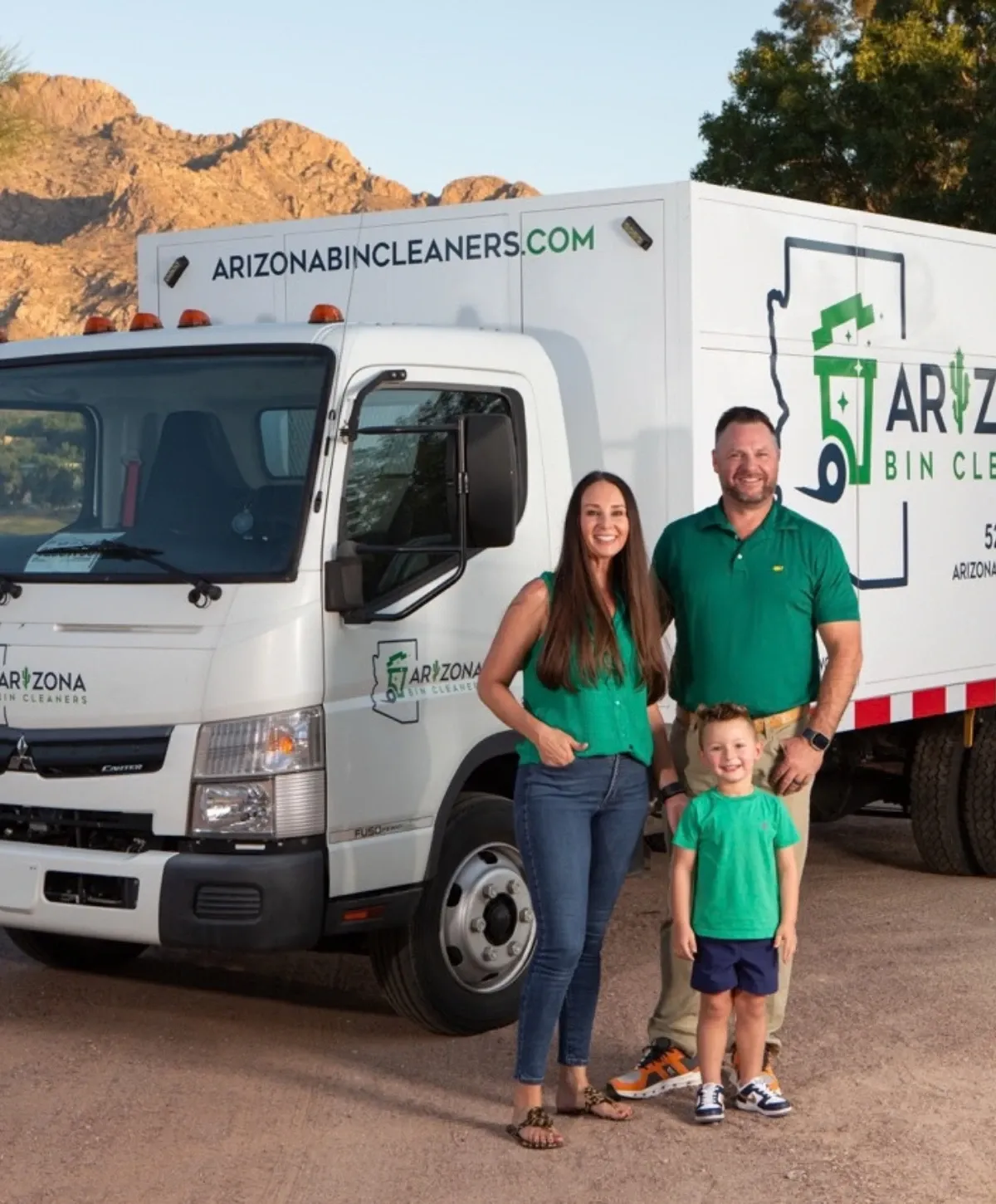 A family of three (man, woman, child) stands smiling in front of a white Arizona Bin Cleaners service truck.