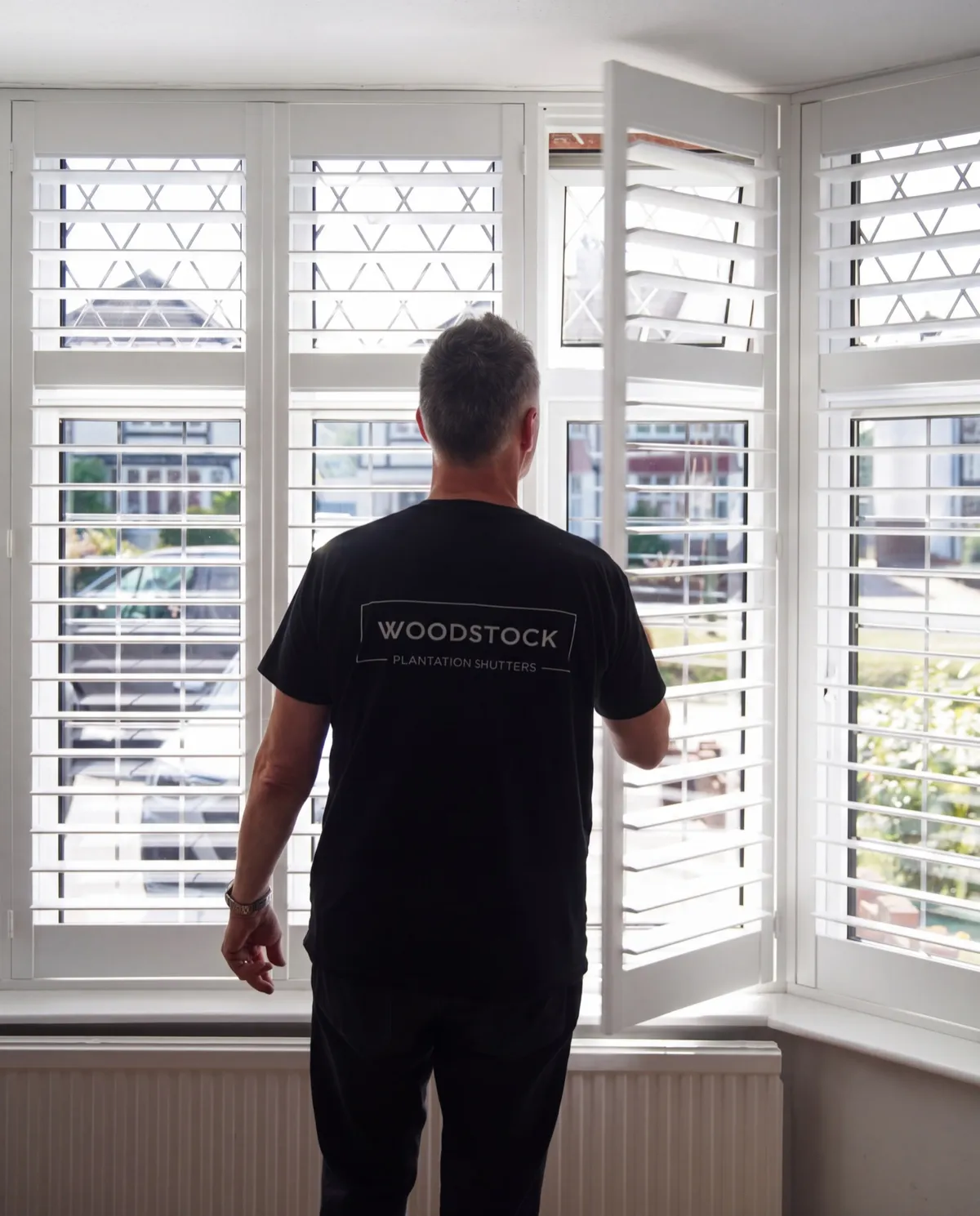 Woodstock Shutters fitter opening white plantation shutters in a bay window