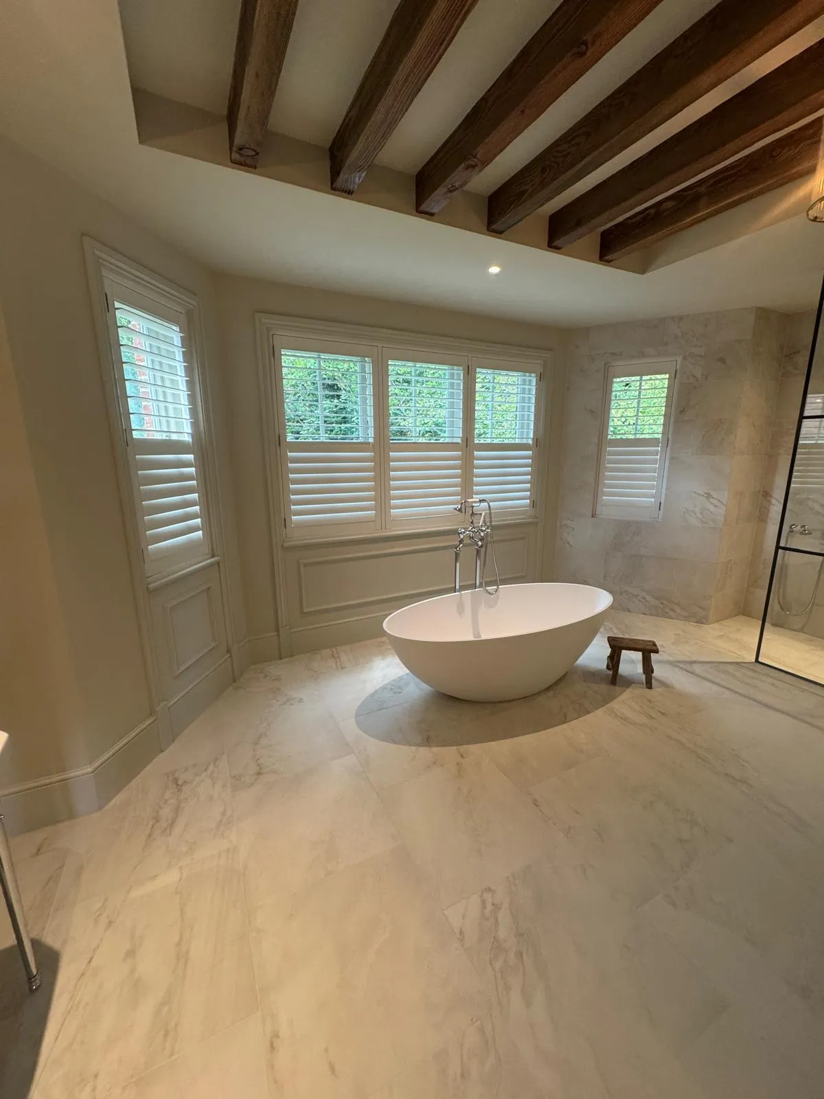 Plantation shutters in a beamed bathroom with a freestanding bath
