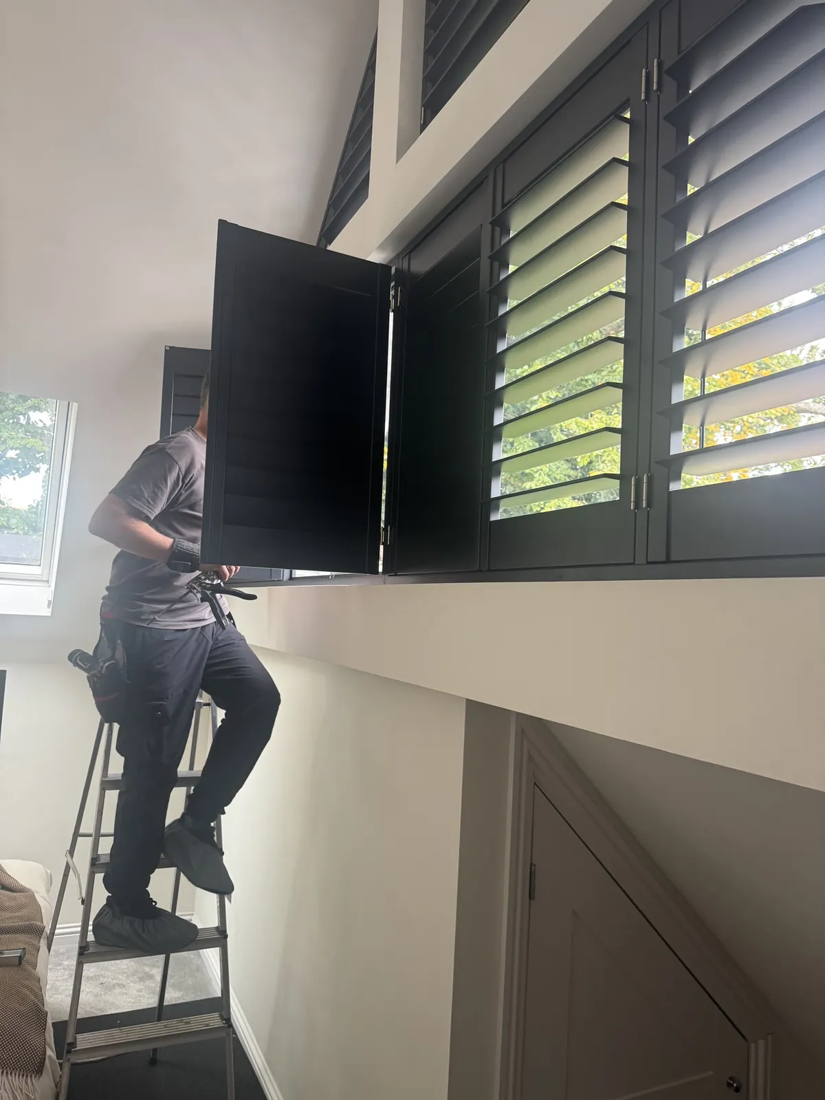 Woodstock Shutters fitter installing dark plantation shutters on a high window