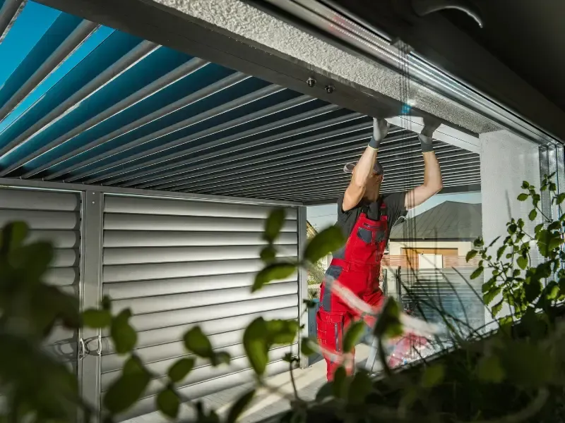 Worker installing metal carport roof panels along the ceiling framing.