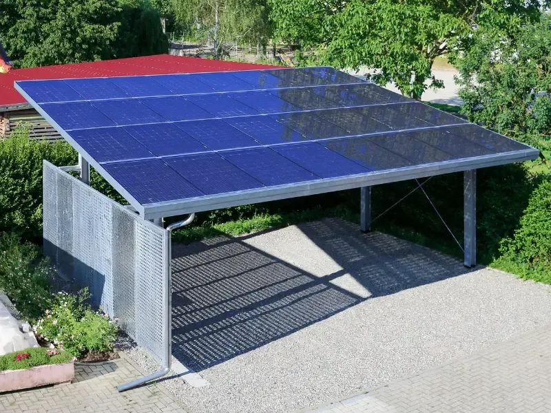 Metal carport with solar panels on the roof over a gravel driveway.