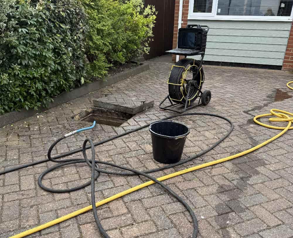 I'll create appropriate alt text for an image showing a manhole with CCTV equipment: "Open manhole during CCTV drain survey in Bournemouth being conducted by 1st Call Drainage technicians to detect blockages or damage.