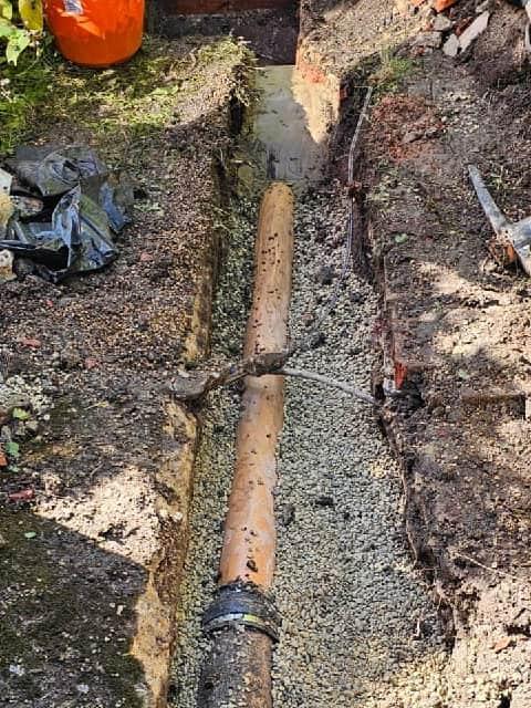 New drainage pipe being fitted to existing pipework during a localised excavation repair.