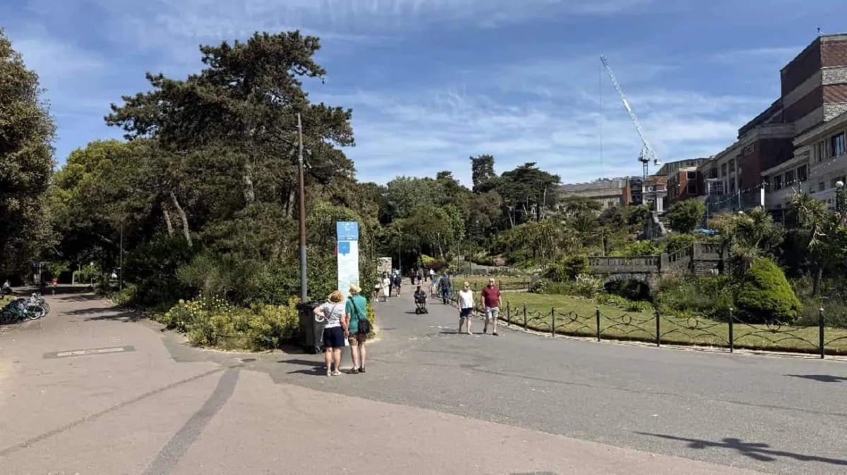 Gardens in Bournemouth showing visitors walking through the landscaped park with mature trees and coastal buildings in the background.