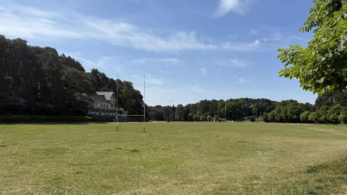 Rugby pitch at Meyrick Park in Bournemouth with goal posts on the field surrounded by mature trees and residential buildings.