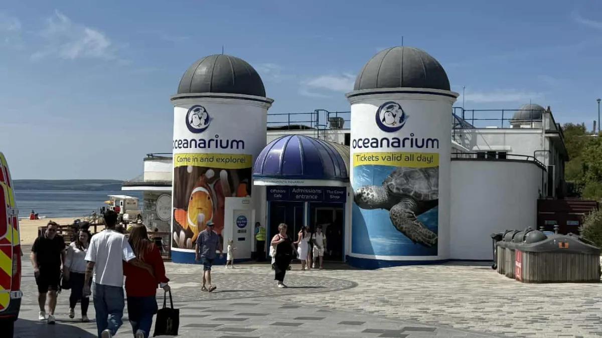 Based on the image you've shared, here's the alt text: "Bournemouth Oceanarium entrance with distinctive twin domed towers and visitors on the seafront promenade.
