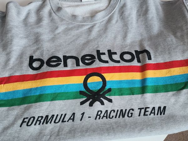 Benetton logo and word over red, yellow, blue green stripe and words Formula 1- Racing Team