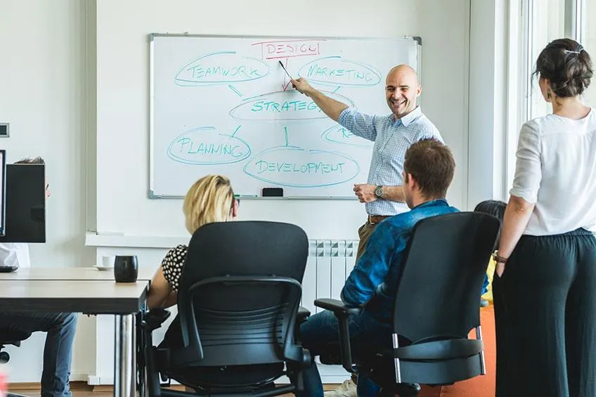 Group meeting with a presenter drawing on a whiteboard and participants watching