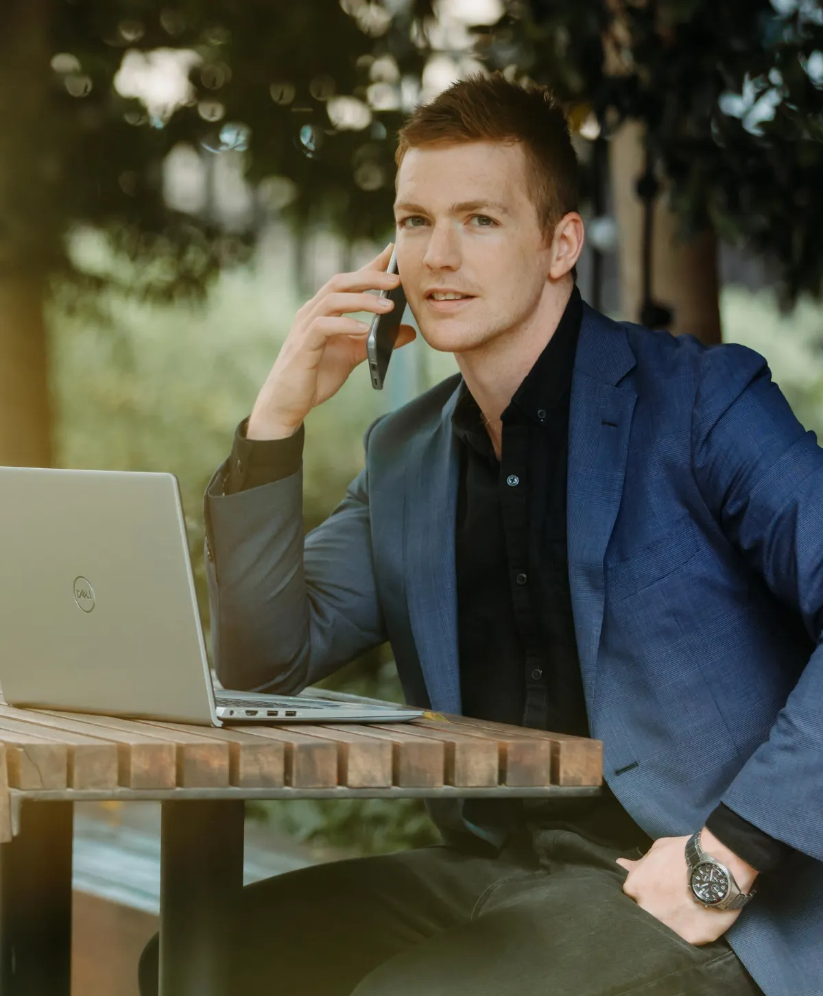 man in corporate coat sitting on  bench answering a phone call