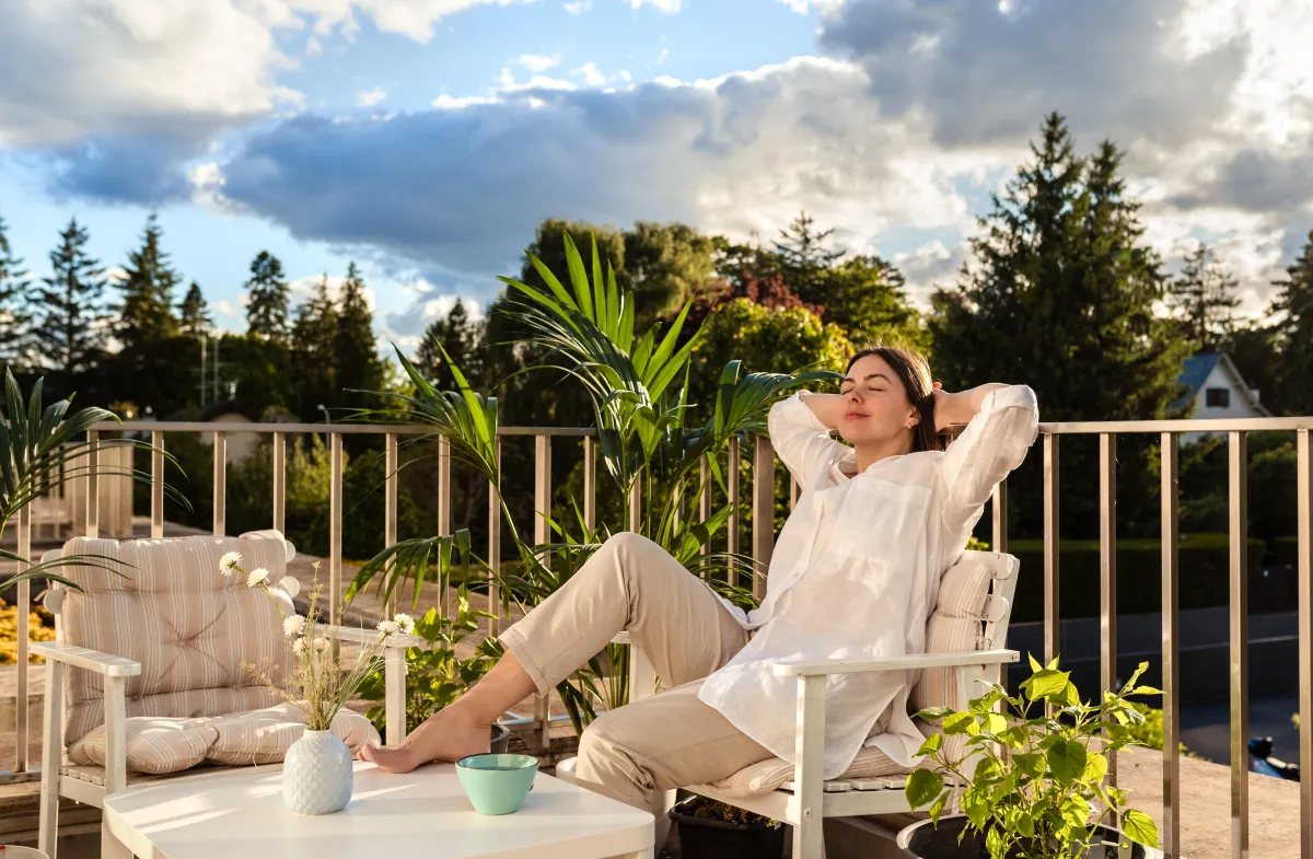 Back of woman sat on top of hill with arms wide, wind blowing behind her