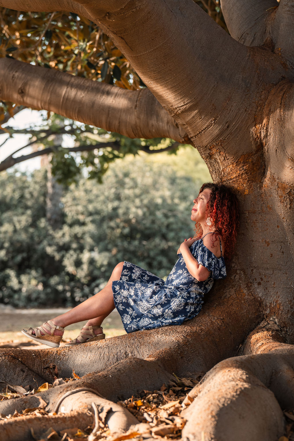 A priestess sitting on roots an leaning against the tree trunk. Reflecting, silence complementation, grounded spirituality.