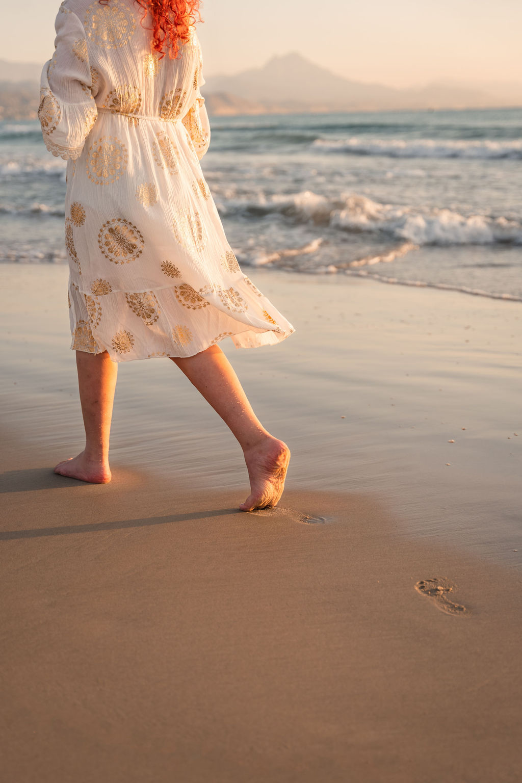 Finding your unique path and daring to follow it step by step is important and truly essential, in our view. This is what we help you with if you wish to co-create with us. Footprints in the sand, ocean waves, a white dress with touches of gold.