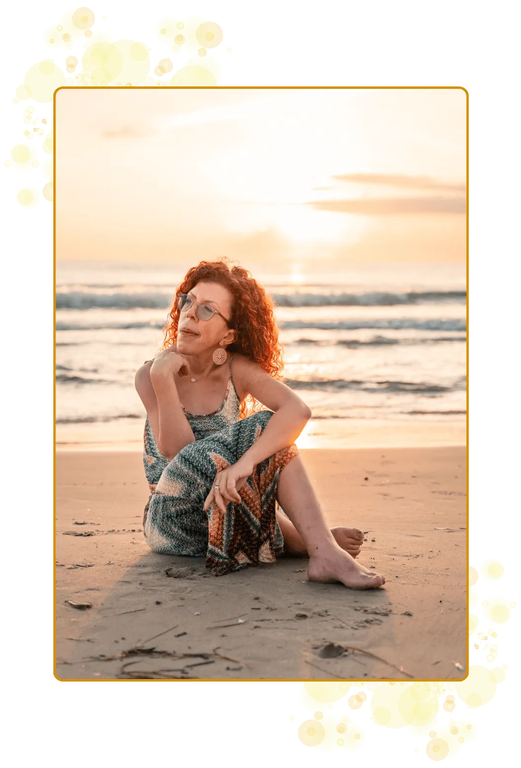 Undrende kvinne sitter på stranden. Bølgende hav og glødende soloppgang i bakgrunnen. Kjole i pastellfarger.