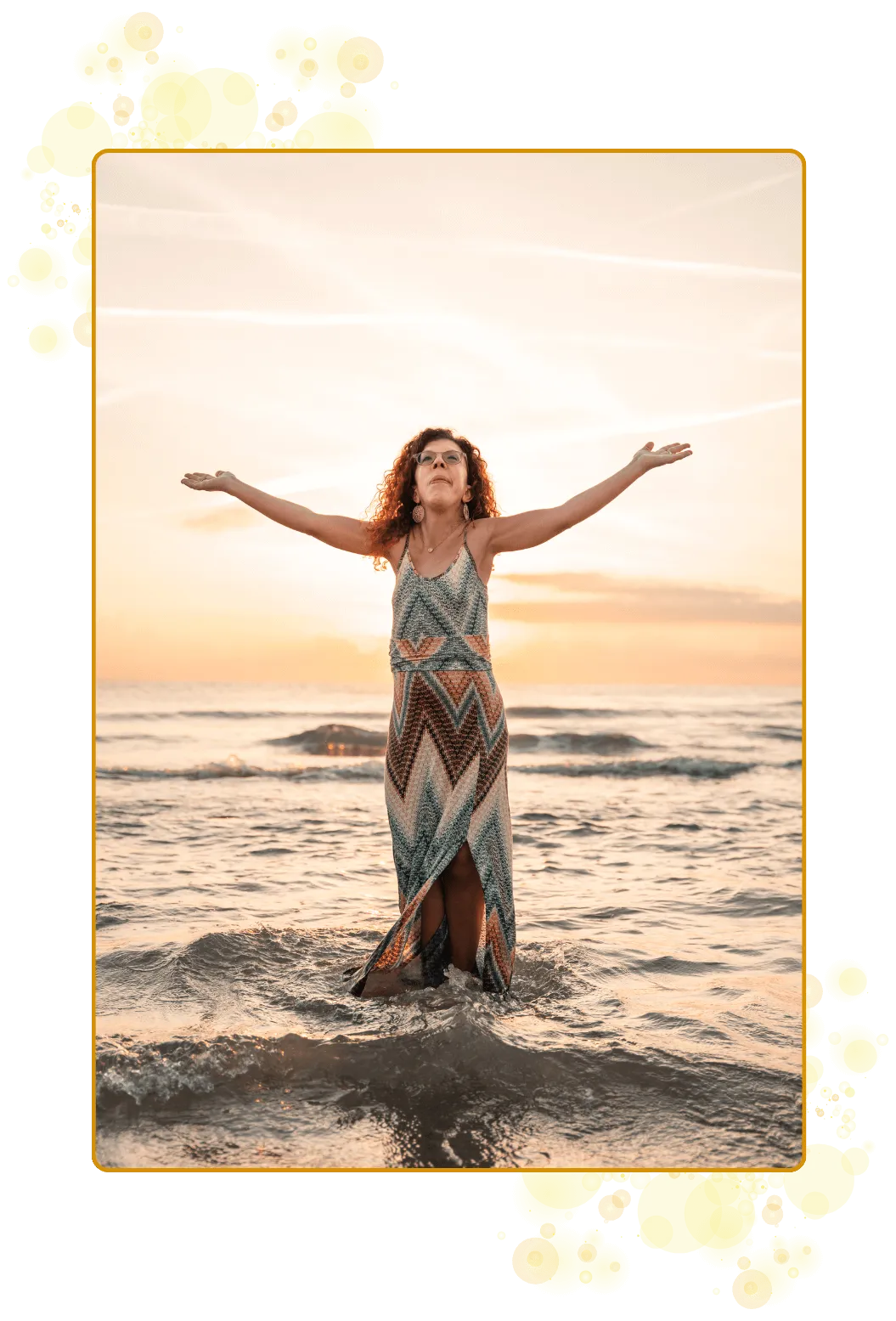 En prestinne med knallrødt og rødt hår, hendene i været, gyllen soloppgang i bakgrunnen og stående i havet med bølgeskvulp rundt seg. Kraftfullt, lysende og et stort JA til kallet sitt.