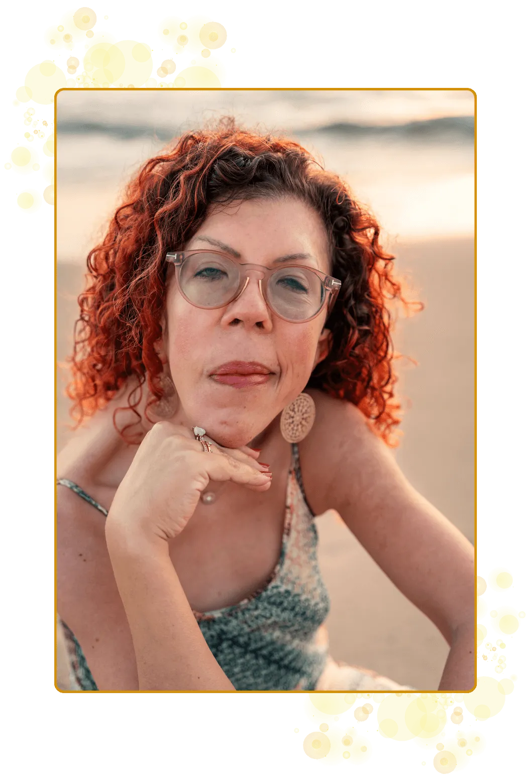 Smilende kvinne, aktivator og frekvensbærer. Sittende på stranden i soloppgangens gylne toner. Rødt, krøllete hår. Briller. Øredobber i gull. Et blikk som møter ditt.