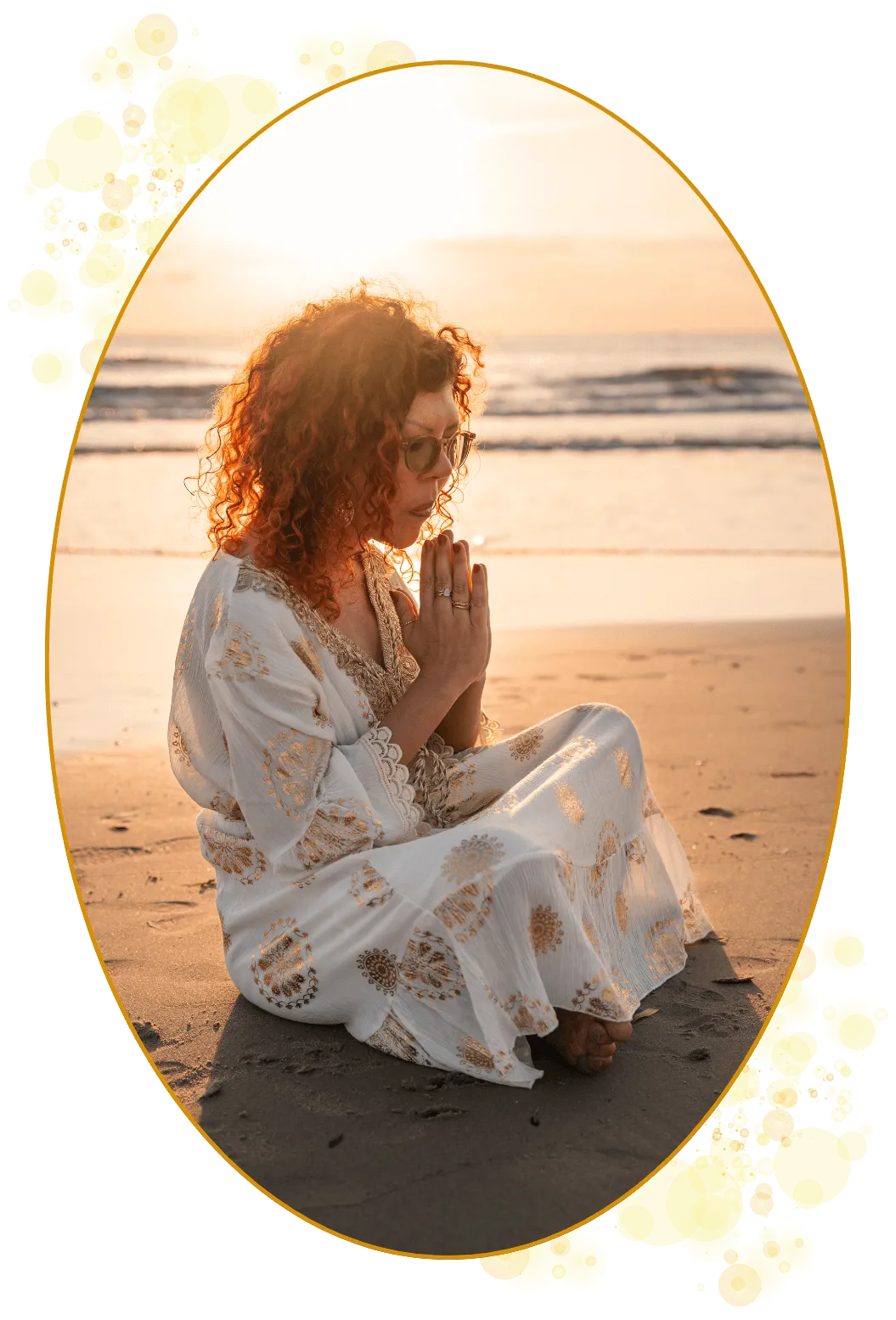 En prestinne holder hendene i en namaste-hilsen. Hun sitter på stranden med brusende hav og gyllen solopgang i bakgrunnen. Hennes røde, krøllete hår gløder. Hun er i forbindelse med seg selv, kroppen, sjelen, Universet og alle de fantastiske lysvesnene som arbeider gjennom henne som kanal og yppersteprestinne.