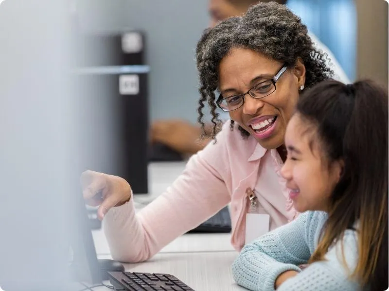 teacher at computer with young asian irl teaching her